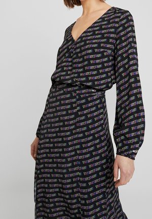 Femme portant une robe noire à manches longues avec un motif de texte coloré "Tommy Jeans", avec un col en V et une ceinture élastique.