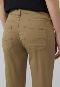 Khaki spodnie w slim fit. Posiadają dwie tylne kieszenie z zaokrąglonym przeszyciem. Wykonane z gładkiego bawełnianego materiału o subtelnym połysku.