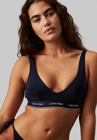 Marine bikini top met een V-hals ontwerp, gemaakt van gladde stof. Heeft een merkband in contrasterend wit, met verstelbare schouderbanden.