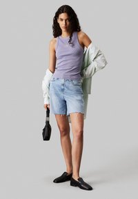 Top morado de canalé, pantalones cortos de denim azul claro con dobladillo deshilachado, camisa blanca oversized colgando del hombro y zapatos negros sin cordones.