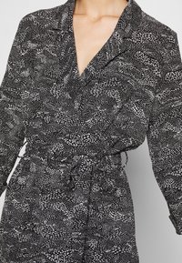 Randig svart och vit klänning med krage, långa ärmar och insvängd midja. Tillverkad av lättviktsmaterial med en texturerad yta.