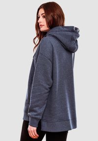 Sudadera gris de gran tamaño en tejido suave, con capucha ajustable, puños de canalé y un dobladillo trasero ligeramente más largo para mayor cobertura.