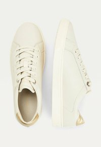 Białe skórzane sneakersy z zaokrąglonym noskiem, płaskimi sznurowadłami, złotymi akcentami na pięcie i teksturowaną gumową podeszwą. Gładki, minimalistyczny design.