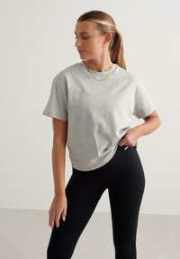Graues Baumwoll-T-Shirt mit kurzen Ärmeln, rundem Halsauschnitt und geprägtem Logo auf der Vorderseite, kombiniert mit schwarzen Rippleggings.