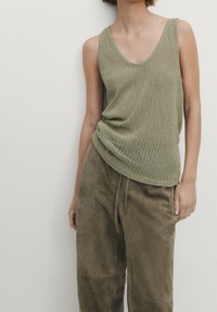 Olive green knit tank top with a scoop neckline, paired with loose, soft olive pants featuring an elastic drawstring waistband.