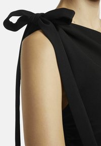 Detail van een zwarte jurk met een geraffineerde schouder en een gestrikt strikje. De gladde stof en de gestructureerde ontwerp accentueren de schouderlijn.
