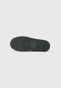 Semelle de sneaker en caoutchouc noir avec une texture, un motif de grip et des détails de logo. Des bords lisses et une forme de bout arrondi améliorent la fonctionnalité.