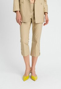 Pantaloni beige cropped con una vestibilità sartoriale. Tessuto liscio, orli arrotolati con bottoni decorativi. Abbinati a tacchi appuntiti gialli lucidi.