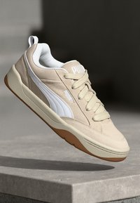 Beige sporta apavi ar teksturētu virsmu, baltām akcentiem un apaļo purngalu. Aprīkoti ar brūnu gumijas zoli un šņorēm, ar subtilu logotipu.