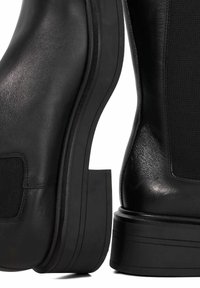 Black leather ankle boots featuring a textured side panel, a thick platform sole, and contrasting smooth leather accents, showcasing a modern design.