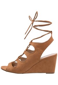 Hnědé semišové klínové sandály s vykrojeným designem, otevřenou špičkou a tkaničkami kolem kotníku. Mají strukturovaný svršek a tvarovanou klínovou podrážku.