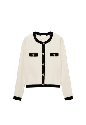 Cardigan crème avec bord noir, col rond et boutons dorés. Équipé de deux poches noires en accent à l'avant. Matière en tricot douce.