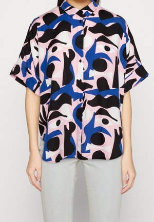 Lyhythihainen nappipaita, jossa mustia, sinisiä ja vaaleanpunaisia abstrakteja kasvokuvioita, yhdistetty vaaleanharmaisiin housuihin.