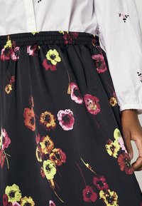 Jupe à imprimé floral avec une base noire, ornée de fleurs rouges, roses et jaunes. Taille élastique et tissu doux et texturé.