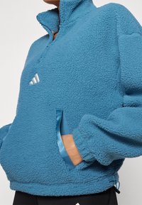 Fleece-pullover i blått med hög krage, halvdragkedja och satinackent vid fickan. Har elastiska manschetter och justerbar nederkant.