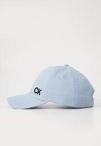 Világoskék baseball sapka pamutból, fekete hímzett "CK" logóval elöl, ívelt szélekkel és szellőzőlyukakkal.