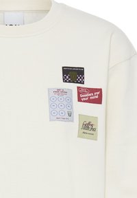Chemise blanche avec quatre patchs colorés : motif tasse de matcha, carte boisson gratuite avec huit cercles, texte sur la santé mentale, et "Coffee" barré pour "Matcha."