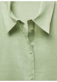 Chemise en lin vert clair avec col pointu et trois boutons beiges attachés sur la patte de boutonnage avant.