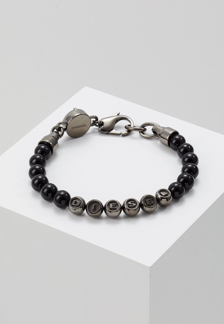 Bracelet avec perles noires alternées et perles lettres métalliques épelant "DIESEL,", fixé avec un fermoir mousqueton argenté et une étiquette ronde de marque.