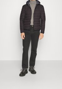 Černá prošívaná bunda s kapucí, zipem na zapínání a žebrovanou texturou, kombinovaná se šedým rolákem, černými d žíny a černými teniskami se vzorovanými tkaničkami.