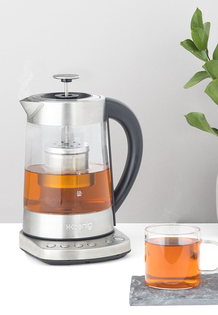 Wasserkocher mit einem Edelstahlboden, einem klaren Glasgehäuse und einem schwarzen Griff. Enthält einen Teesieb und zeigt Messmarkierungen an.