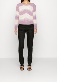 Pull en tricot rayé violet clair et crème avec un col côtelé, associé à un pantalon noir ajusté et des sandales noires à lanières.
