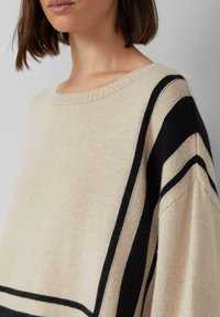 Beżowy sweter dziewiarski w czarne paski. Żebrowany dekolt i szerokie rękawy. Miękka tekstura, lekki materiał.