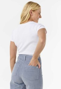 Cropped top bianco a maniche corte abbinato a pantaloni in corduroy azzurri chiari a vita alta, dotati di due tasche posteriori e un motivo testurizzato.
