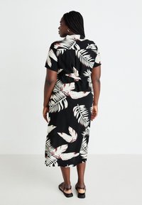 Black dress with short sleeves, featuring white and red leaf patterns, waist tie, and a mid-length hem. Smooth fabric, relaxed fit.