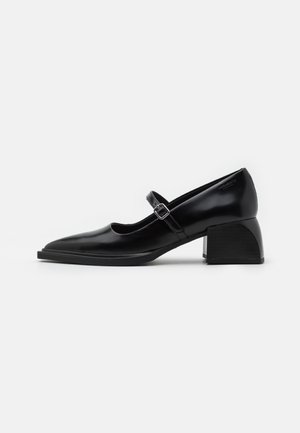 Black leather Mary Jane shoe with a square toe, adjustable strap, and chunky block heel on a white background.