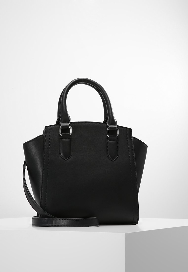 Sac à main structuré noir avec doubles poignées supérieures, ferrures argentées et une bandoulière amovible sur un piédestal blanc.