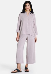 Camicia di lino lilla chiaro con bottoni frontali e maniche a tre quarti, abbinata a pantaloni larghi e svasati dello stesso colore. Sandali neri completano il look.