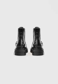 Black leather ankle boots feature a chunky sole, side zippers, and a smooth texture. The design includes minimalist stitching and a sturdy build.