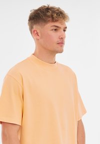 Korte mouwen t-shirt van zacht perzikkleurig materiaal, met een klassieke ronde hals en een ontspannen pasvorm. Glad textuur zonder patronen of accenten.