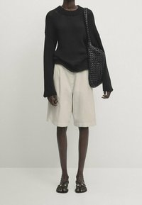 Mustavillasukkoinen neule, vaaleanbeiget sortsit ja mustat hihnasandaalit. Laukku on kudottu tekstuurilla, joka täydentää asun värejä.