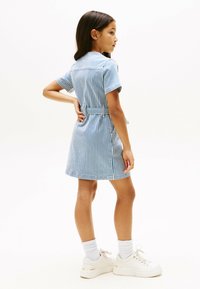 Abito corto a strisce blu e bianche con maniche corte, vita con cintura e tasche laterali. Abbinato a scarpe da ginnastica bianche e calzini alla caviglia.