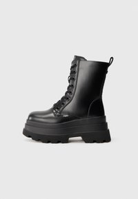 Botas de tobillo negras con cordones y suela de plataforma gruesa, acabado de cuero suave y tirador. Cuenta con ocho ojetes y suela texturizada.