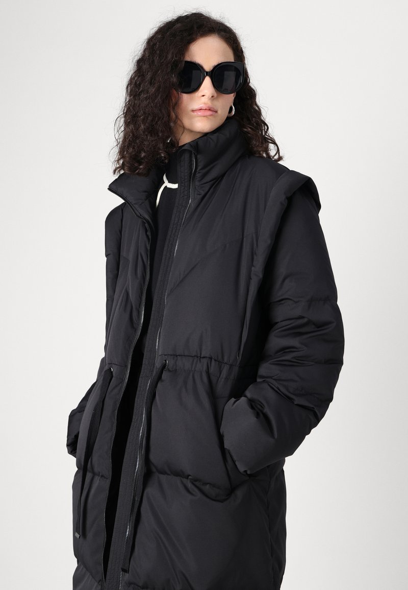 Schwarze Pufferjacke mit hohem Kragen, Reißverschluss und elastischem Bund. Verfügt über Seitentaschen und eine glatte, glänzende Textur.