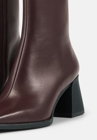 Burgundy leather ankle boot with a smooth finish, featuring a square black heel and a side zipper for closure.