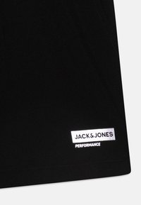 Juodos sportinės šortai su lygiu paviršiumi, su balta "JACK & JONES PERFORMANCE" etikete apatine dalimi ir tvarkingais siuvimo detalėmis.