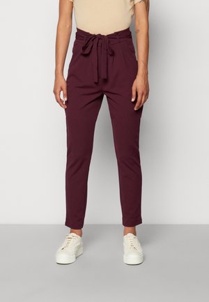 Burgundy Hosen mit Taillenkordel, schmal zulaufenden Beinen und umgeschlagenen Säumen, aus glattem Stoff, kombiniert mit weißen Turnschuhen.