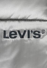 Sivi materijal s logom "Levi's" u tamnoplavoj vezici, jasno ušiven s glatkom, sjajnom teksturom.