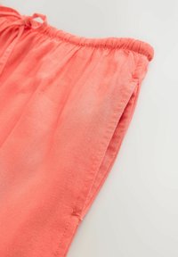 Lněná látka v korálové barvě s elastickým pasem a šňůrkou na stažení. Uvolněný střih se záhyby po stranách. Hladká textura.