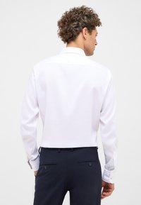 Witte lange mouwen shirt met een gladde textuur, rugpasdetail en met knopen aan de manchetten, gecombineerd met donkerblauwe broeken met achterzakken.
