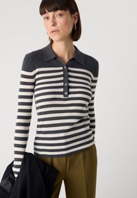 Polo en maille à rayures à manches longues bleu marine et crème. Il présente une texture côtelée, un col à boutons et des rayures horizontales.