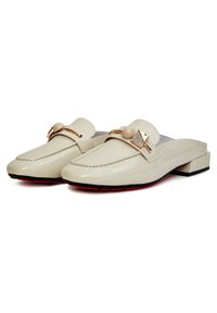 Cremefarbene Patentschuh-Loafer mit niedrigem Blockabsatz, die über ein dekoratives goldfarbenes Hardware-Detail und eine strukturierte Gummisohle mit roten Akzenten verfügen.