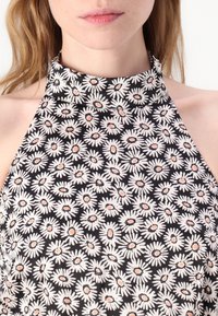 Black sleeveless top with a high neckline, featuring a daisy pattern in white and pink on a dark background. Smooth fabric texture.
