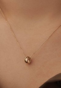 Collier doré avec des pendentifs circulaires entrelacés, suspendu à une chaîne délicate. Texture lisse, design minimaliste et éclat subtil.