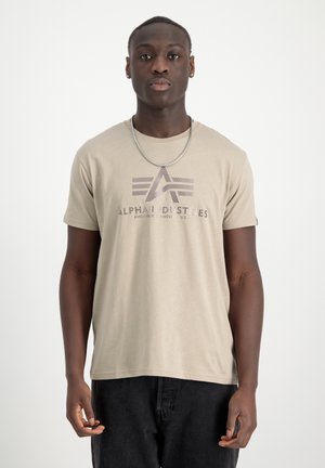 Beige Baumwoll-T-Shirt mit kurzen Ärmeln, ausgestattet mit einem grafischen Logo und dem Text "ALPHA INDUSTRIES" in dunkelgrau auf der Vorderseite.