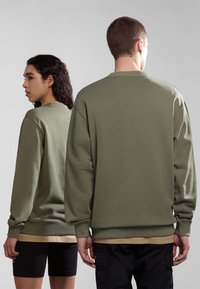 Felpe verde oliva con maniche lunghe, polsini a coste e collo tondo. Entrambi indossano pantaloni shorts neri e uno strato beige sotto.